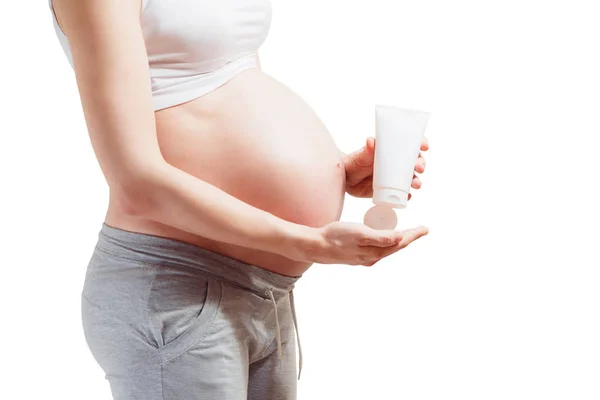 怀孕的年轻女人大肚皮挤压着有用的奶油 — 图库照片