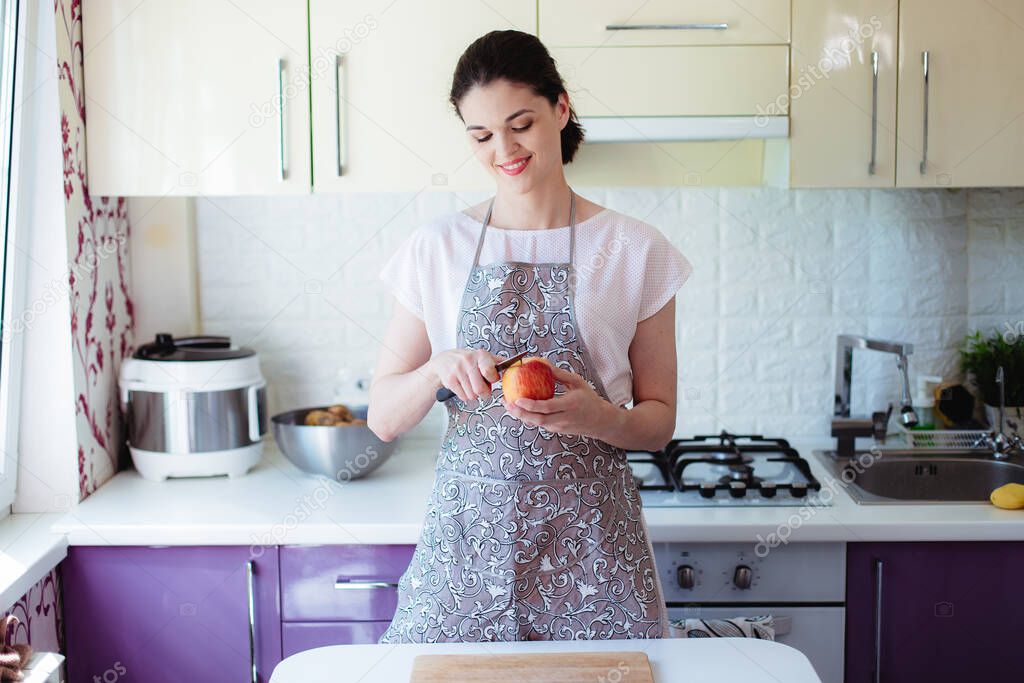 Young woman in the kitchen peels and slices an apple