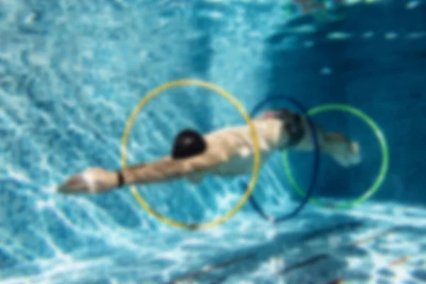 キャップと水泳ゴーグルの男性トレーナーは ぼかしでリングと水の下で演習を行う — ストック写真