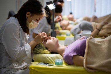 Efendi müşteriye büyük renkli kirpikleri biriktirir. Güzellik fotoğrafçılığına hazırlık. Bir resim oluşturuluyor.