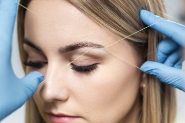 Kozmetik uzmanı müşterinin kaşlarını iplikle yoluyor