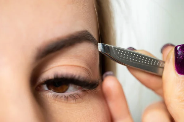 Cosmetologist plucks client eyebrows by tweezers