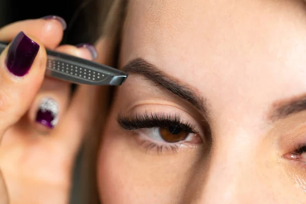 Cosmetologist plucks client eyebrows by tweezers