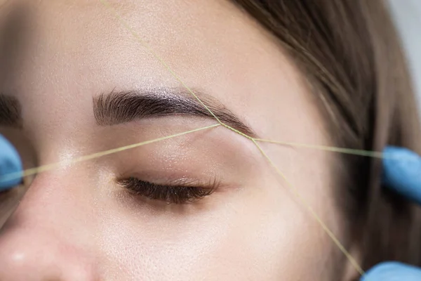 Cosmetologist plucks client eyebrows by thread