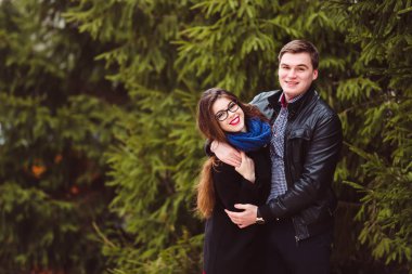 Köknar ağaçlarının arka planında kucaklaşan sevgi dolu çift