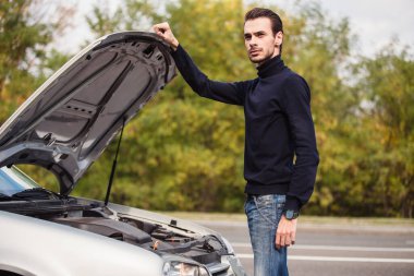 Bir adam yolda arabayı tamir etmeye çalışıyor. 