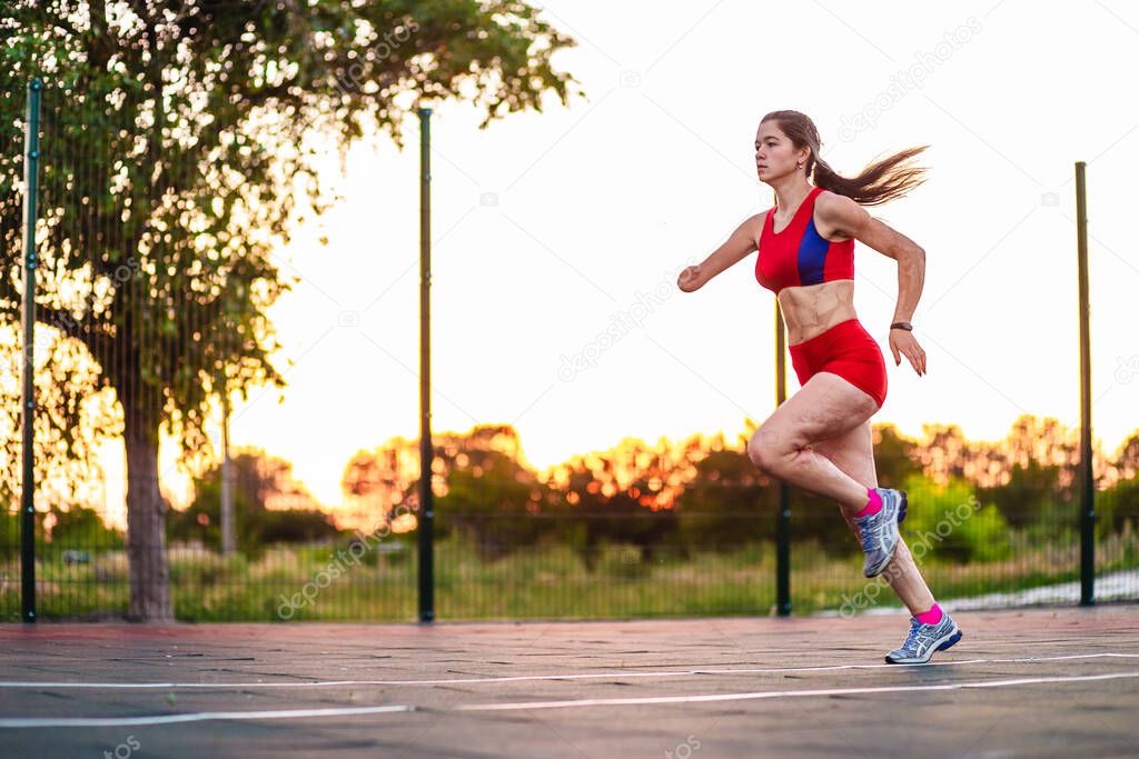 Young woman athlete with an amputated arm and burns on her body runs around the sports field. Outdoor workout.