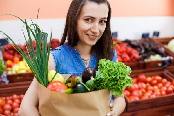 Beautiful young girl with a paper bag with shopping in a vegetab