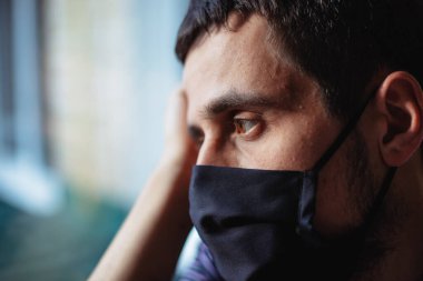 Karantina sırasında bir adam evde tecrit altında kalır. Koronavirüs salgını. Adam pencereden sokağa doğru bakıyor.