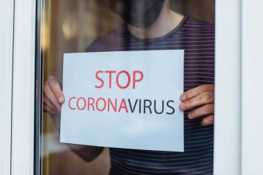 Karantina sırasında bir adam evde tecrit altında kalır. Koronavirüs salgınını durdurun. Adam pencereden sokağa doğru bakıyor.
