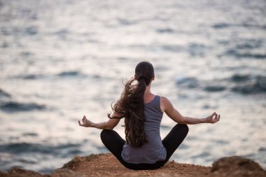 Yogi kızı deniz kıyısındaki bir uçurumda lotus pozisyonunda.