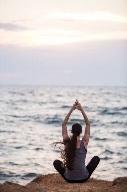 Gün batımında deniz kenarında yoga yapan bir kızın silueti.