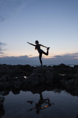 Gün batımında deniz kenarında dans eden bir kızın silueti.