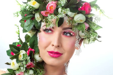 Güzel bir esmerin portresi. Kocaman kirpikleri var. Beyaz bir arkaplanda gül çelengi var..