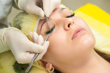 Efendi müşteriye büyük renkli kirpikleri biriktirir. Güzellik fotoğrafçılığına hazırlık. Bir resim oluşturuluyor.