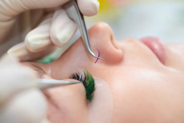 Efendi müşteriye büyük renkli kirpikleri biriktirir. Güzellik fotoğrafçılığına hazırlık. Bir resim oluşturuluyor.