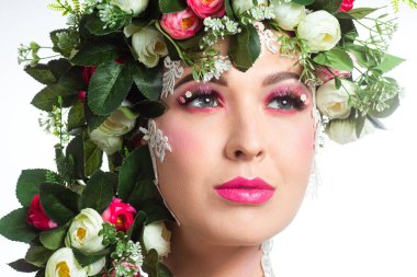 Güzel bir esmerin portresi. Kocaman kirpikleri var. Beyaz bir arkaplanda gül çelengi var..