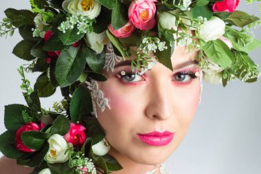 Güzel bir esmerin portresi. Kocaman kirpikleri var. Beyaz bir arkaplanda gül çelengi var..