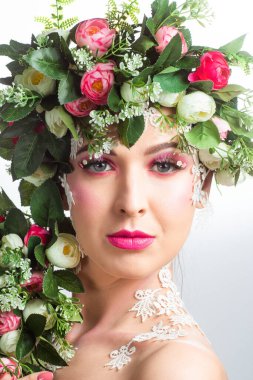 Güzel bir esmerin portresi. Kocaman kirpikleri var. Beyaz bir arkaplanda gül çelengi var..