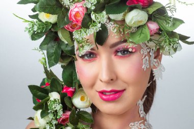 Güzel bir esmerin portresi. Kocaman kirpikleri var. Beyaz bir arkaplanda gül çelengi var..