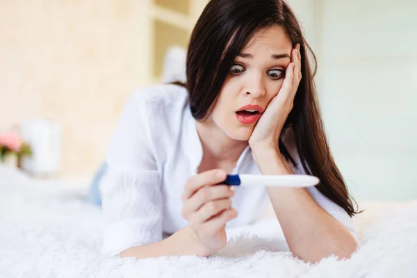 A young woman is shocked and sad when she sees a positive pregnancy test.