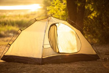 Gün batımında nehir ve ormanın arka planında turist çadırı