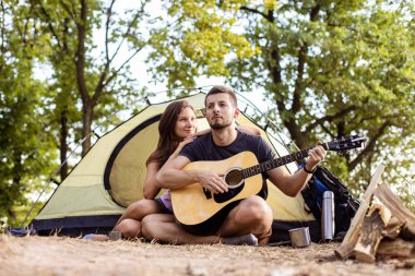 Bir adam gün batımında çadırın yanında gitar çalan bir kadın için çalar. Yürüyüşte balayı.