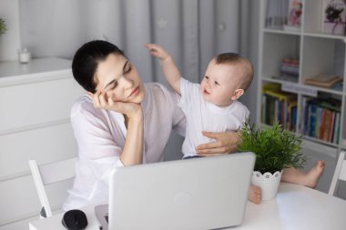 Uykulu bir anne kollarında kaprisli bir çocukla çalışmaya çalışır. Bir kadın baş ağrısı çeker.