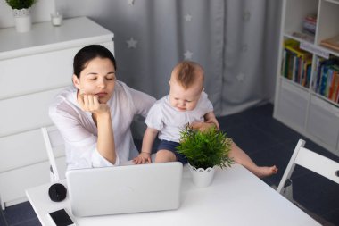 Uykulu bir anne kollarında kaprisli bir çocukla çalışmaya çalışır. Bir kadın baş ağrısı çeker.