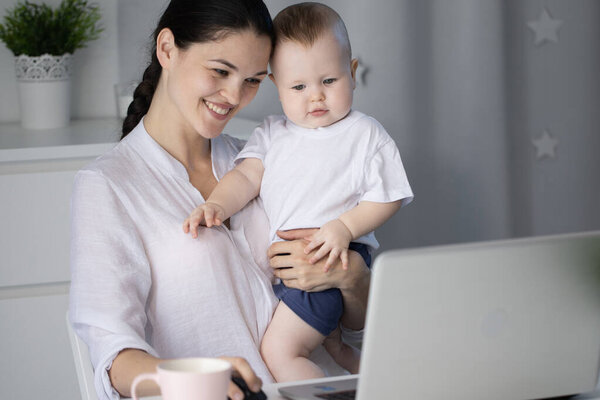 Young mother working in a decree at the computer with a baby son in her arms