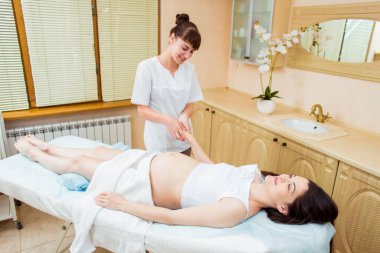 Uzun saçlı güzel hamile esmer kadın kozmetoloji odasında ellere masaj yapmaktan hoşlanıyor.