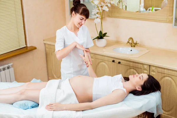 Beautiful pregnant brunette woman with long hair enjoys a pinch massage of hands in a cosmetology room