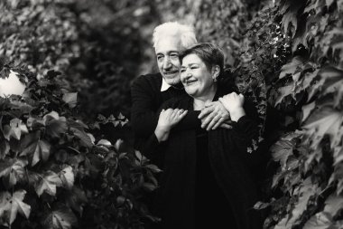 Sonbahar parkında birbirine aşık yaşlı bir çift yürüyor. Yaşlı insanlar birbirlerine sarılırlar. Siyah beyaz fotoğraf.