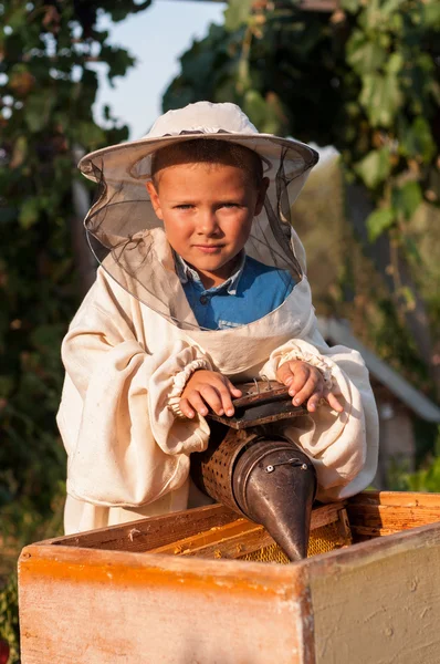 Imker-Porträt eines kleinen Jungen, der im Bienenstock mit Raucher für Bienen in der Hand arbeitet — Stockfoto