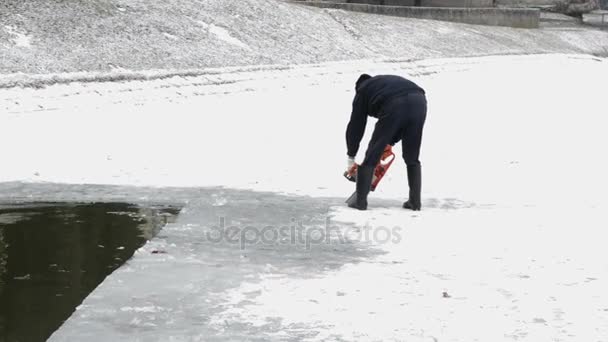 Человек режет лед бензопилой на замерзшем озере — стоковое видео