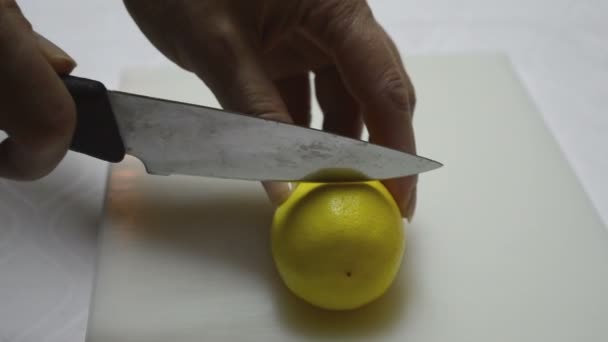 Las manos de las mujeres cortan rodaja de limón con cuchillo en una mitad — Vídeos de Stock