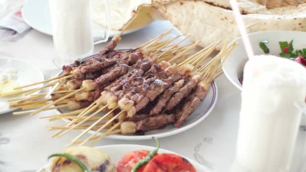 Жареное мясо шашлык с шампуром на тарелке и традиционный турецкий напиток Айран. Клиенты, берущие кебабы руками в ресторане — стоковое видео