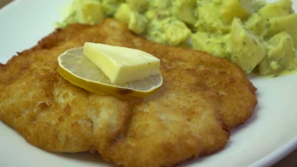 Schnitzel, pollo frito crujiente, rodaja de limón y mantequilla con ensalada de patata, girando en plato — Vídeos de Stock