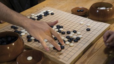 Hand playing black and white stone pieces on Chinese Go or Weiqi game board. Indoor activity with artificial light. clipart