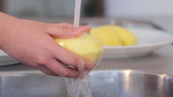 Vrouwelijke handen wassen aardappelen in de keuken gootsteen. Water komt op vers geschilde aardappelen. — Stockvideo