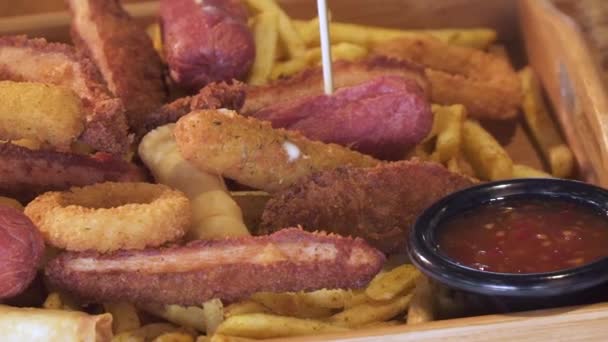 Sausages, onion rings, fried chicken, schnitzel and french fries. Food bucket with full of fried fast food. Traditional beer snack. Close up, pan shot. — Stock Video