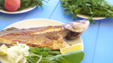 Soğan, dilimlenmiş limon ve Bahçe roket aragula mavi masaya ile plaka üzerinde deniz levreği ızgara. Yunan yemeği.