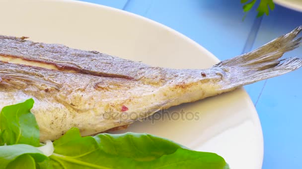 Orata grigliata su piatto con limone, rucola, fetta di limone e cipolle. Cibo sano. Sfondo tavolo blu . — Video Stock