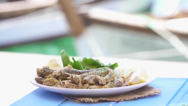 Turco Hamsi Tava com limão e arugula na mesa azul. Anchovas fritas junto ao mar em Foca Izmir. Espaço de cópia com fundo mar e barcos pequenos . — Vídeo de Stock