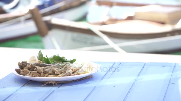 Turecká Hamsi Tawa s citronem a rukolou na modrém stole. Smažené ančovičky u moře na Foca Izmir. Kopírování prostor s mořem a malé čluny pozadí. — Stock video