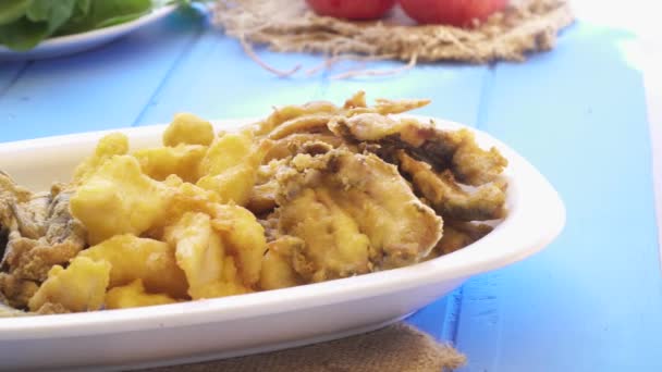 Bouquet de petits poissons frits dans une assiette. Vue macro rapprochée sur la table bleue de style grec . — Video