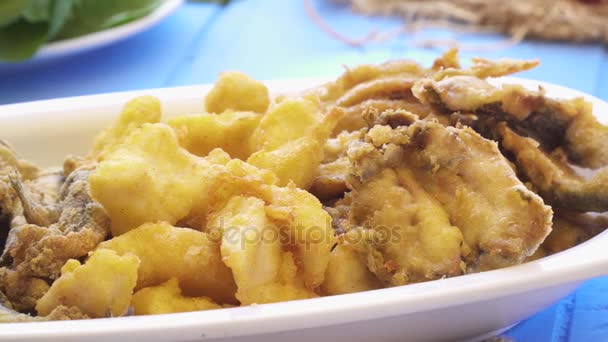 Bouquet de petits poissons frits dans une assiette. Vue macro rapprochée sur la table bleue de style grec . — Video