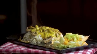 Lezzetli beyaz pirinç, sağlıklı marul salatası, rendelenmiş havuç, sıcak turşu ve siyah çanak üzerinde hizmet veren kaşar soslu baharatlı kızarmış tavuk. Dönen atış.