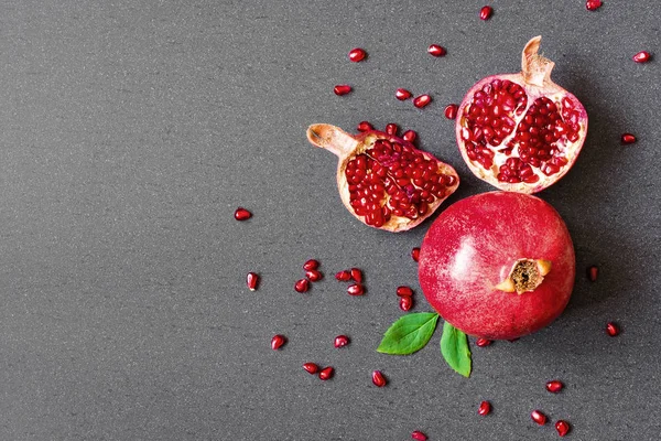 Granada madura y fruta en rodajas con semillas en piedra gris — Foto de Stock