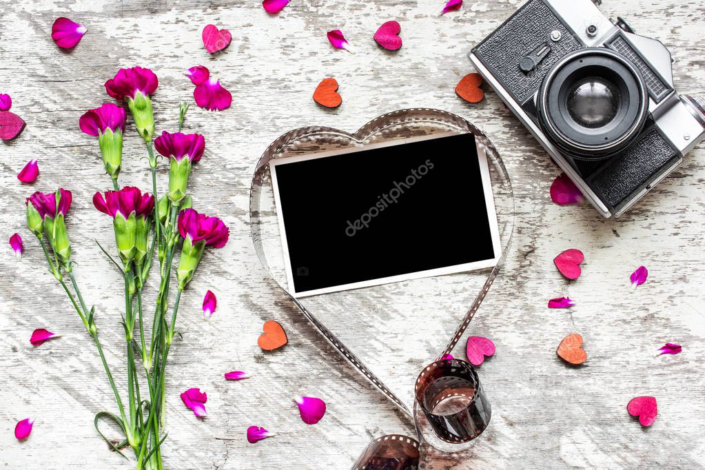 blank photo frame in heart shaped film with retro camera and carnation flowers